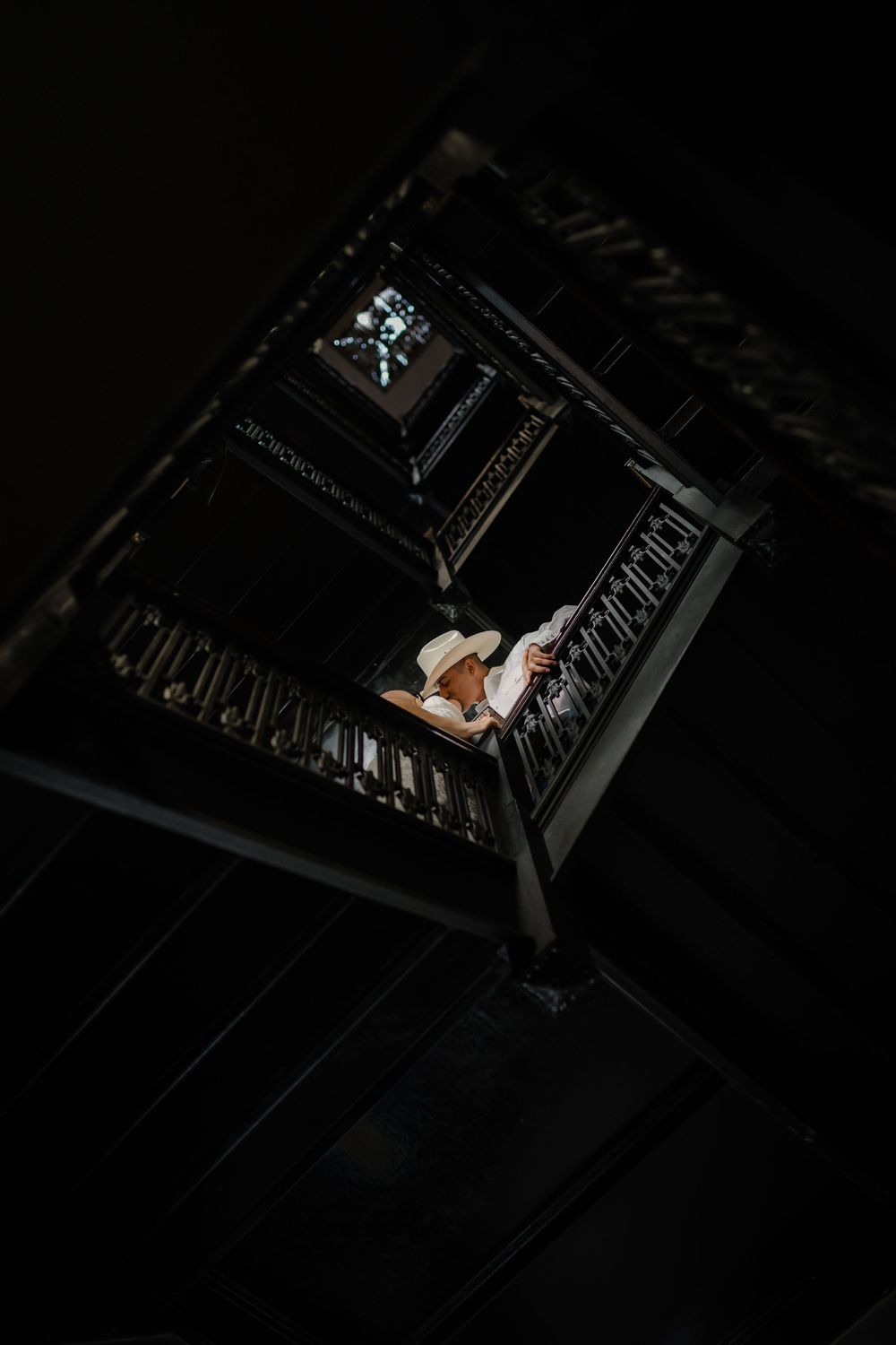 Looking down a dark spiral staircase with dramatic lighting illuminating the steps from above.