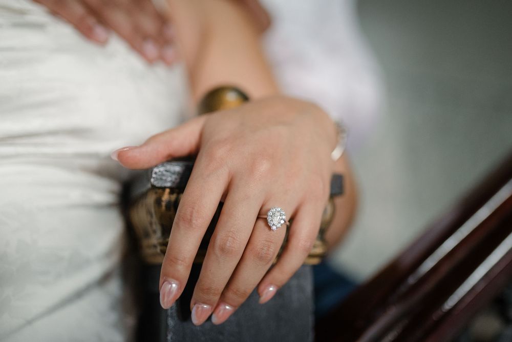 A close-up shot of a hand wearing an elegant diamond engagement ring on a white fabric background.