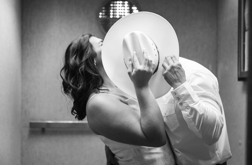 A romantic black and white photograph shows a couple sharing a kiss behind a dinner plate.