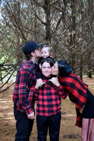 A family wearing matching buffalo plaid shirts poses together in a pine forest setting.