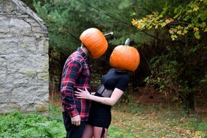 A couple in fall attire poses for engagement photos while holding a pumpkin in a rustic outdoor setting.