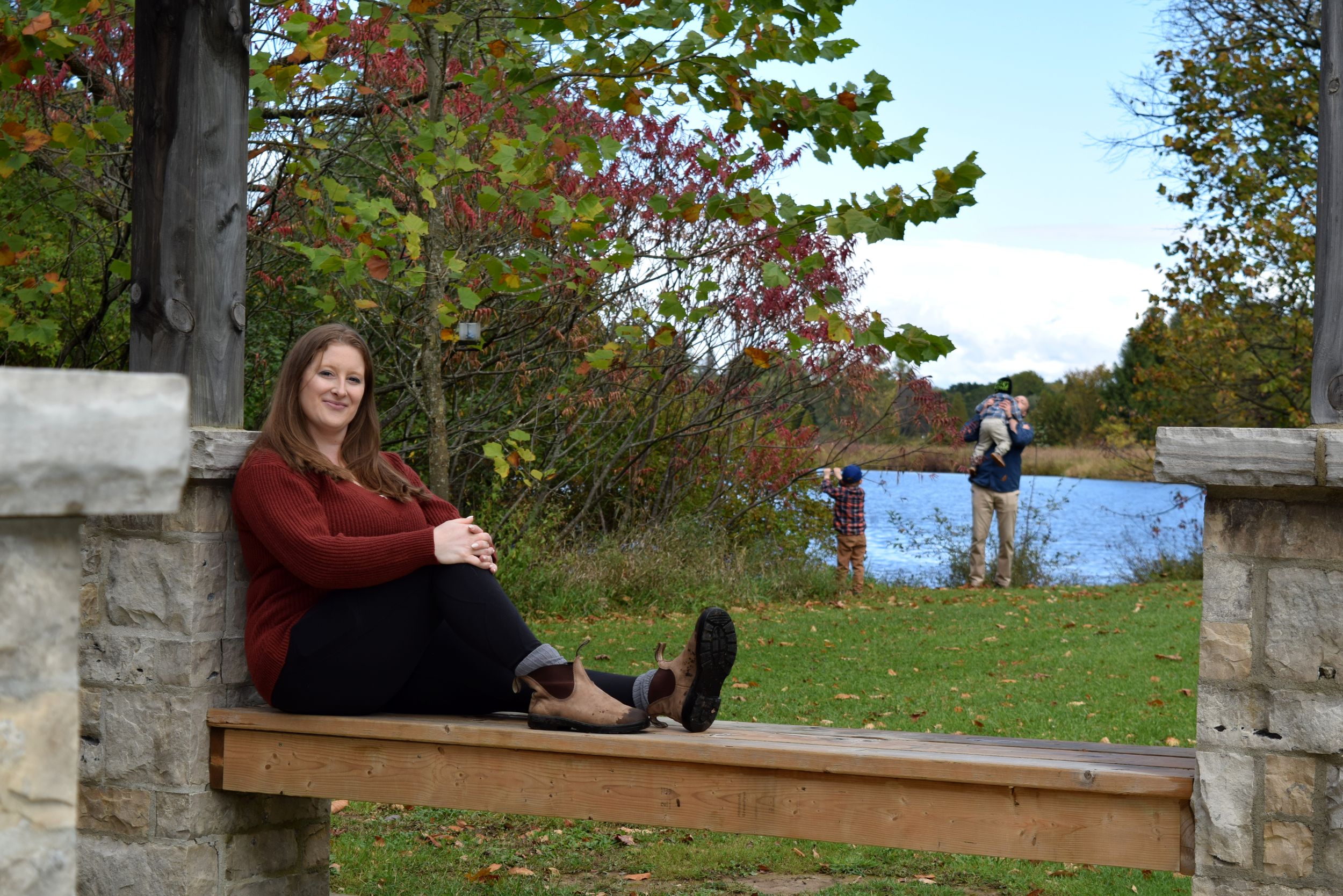 Two people sit together on a wooden bench overlooking a scenic autumn landscape with colorful fall foliage.