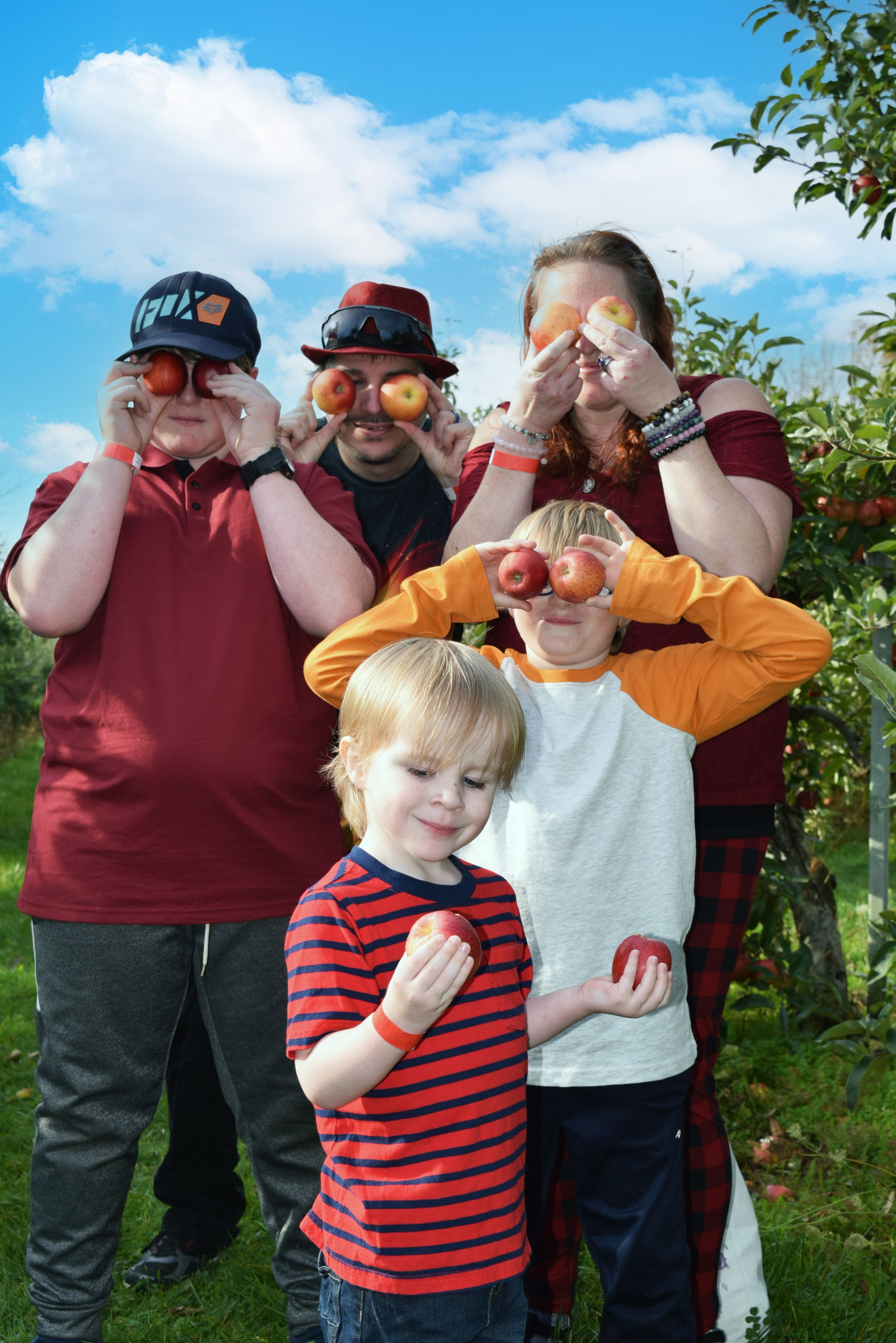 Four people standing in a vineyard or orchard making silly gestures and poses in a playful sequence of photos.