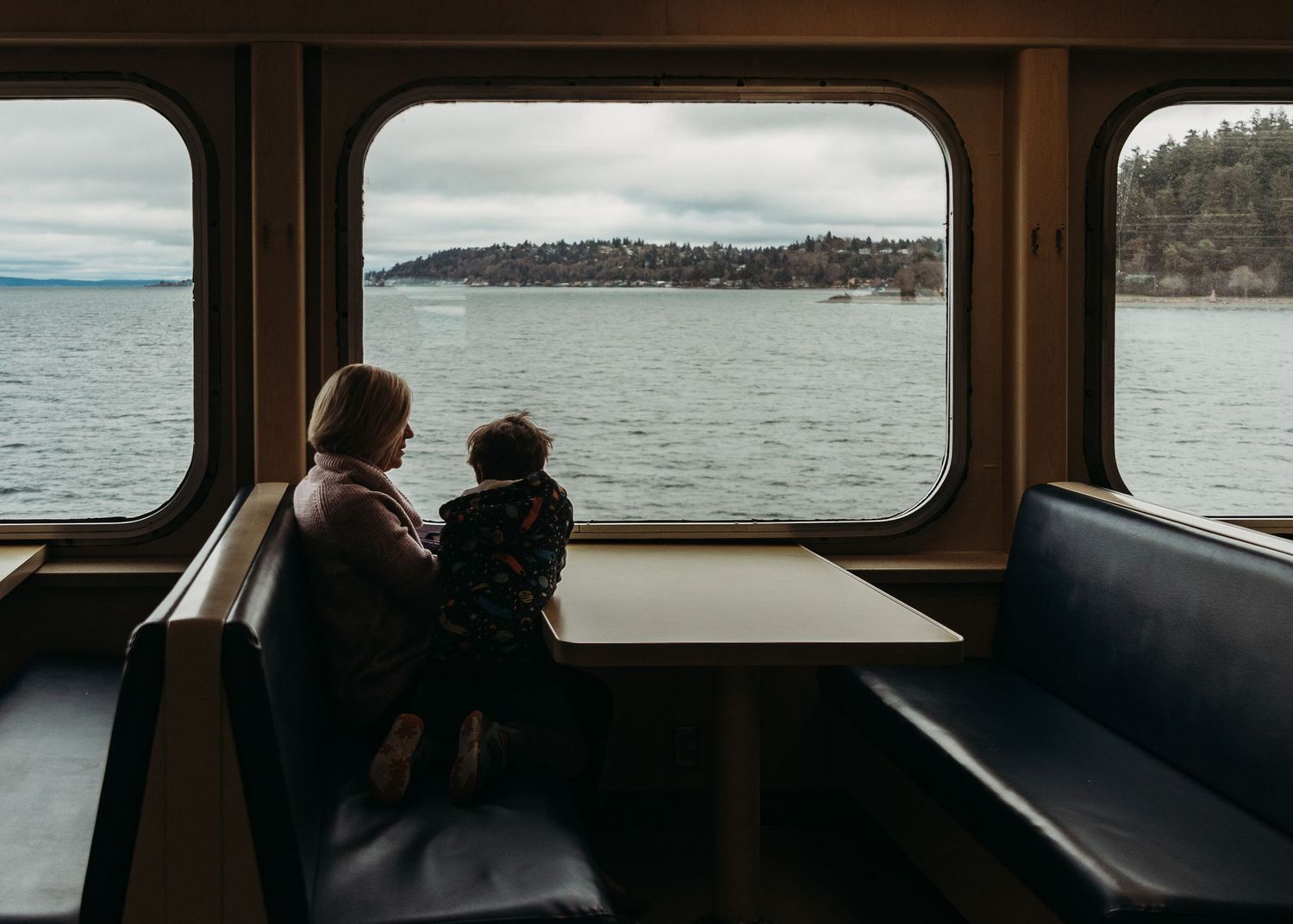 A series of five panoramic windows on a ferry boat showing views of water and distant shoreline.