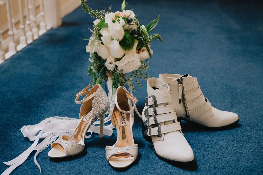 Bridal shoes and bouquet display featuring strappy heels, buckle booties, and white floral arrangement on blue carpet.