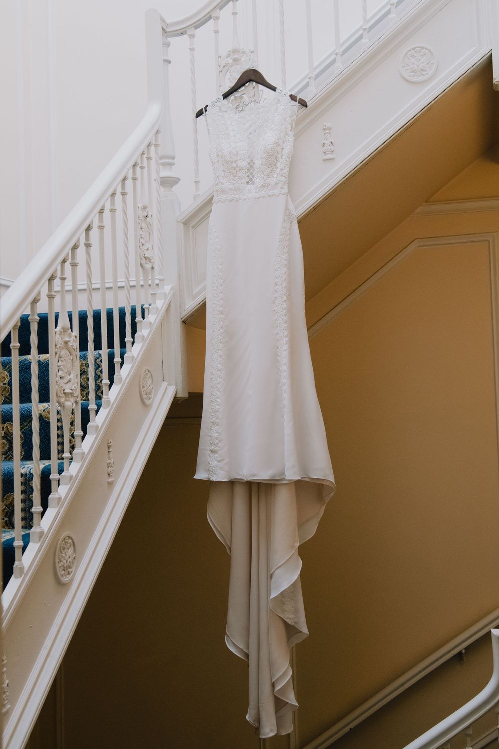 Elegant white lace wedding gown hanging on a staircase railing in a classic venue.