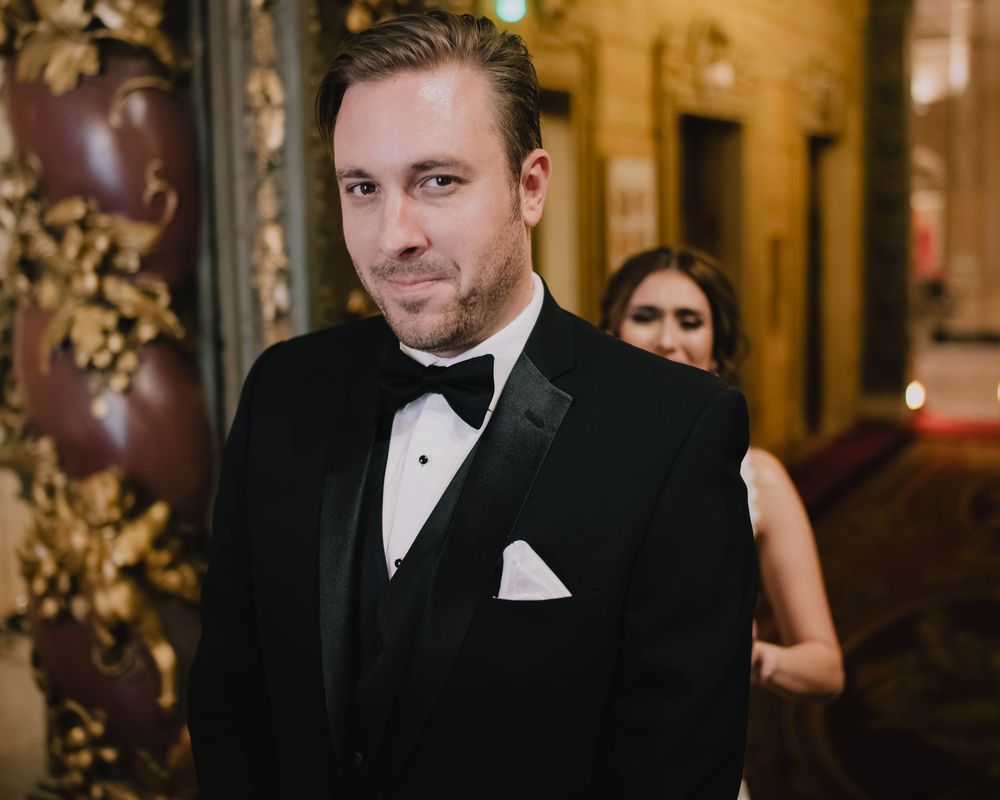 Elegant man in black tuxedo with bow tie and white pocket square at formal event.