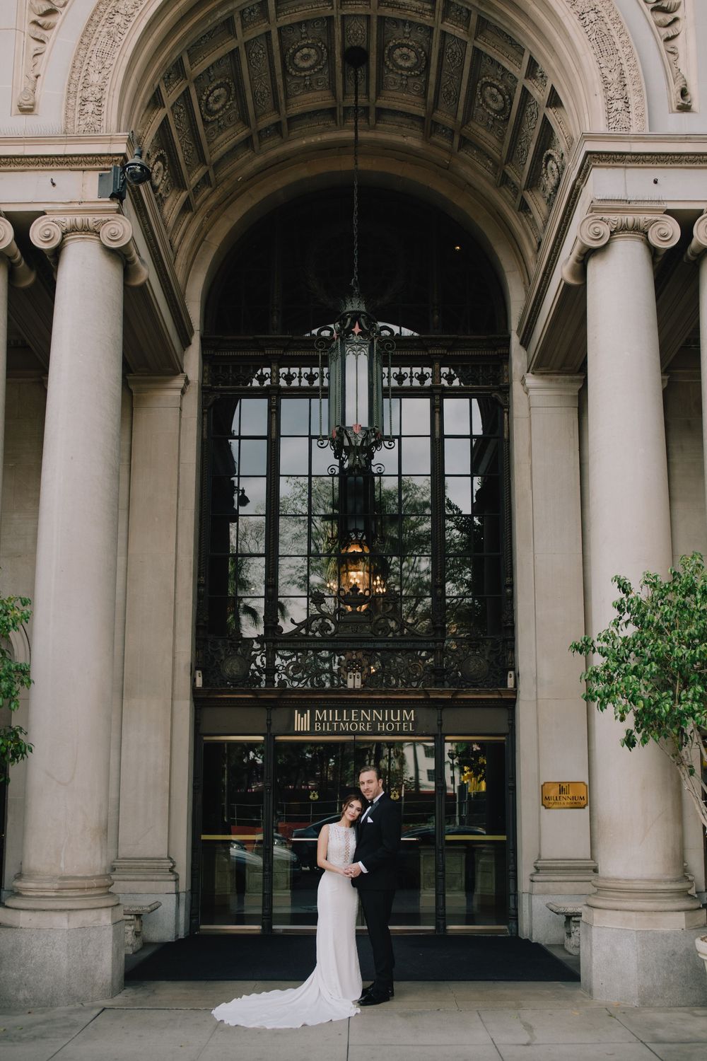 Bride and groom posing at entrance of Millennium Biltmore Hotel under grand archway.