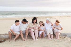 Newcastle newborn baby photographer capturing new mother holding baby at the beach surrounded by family