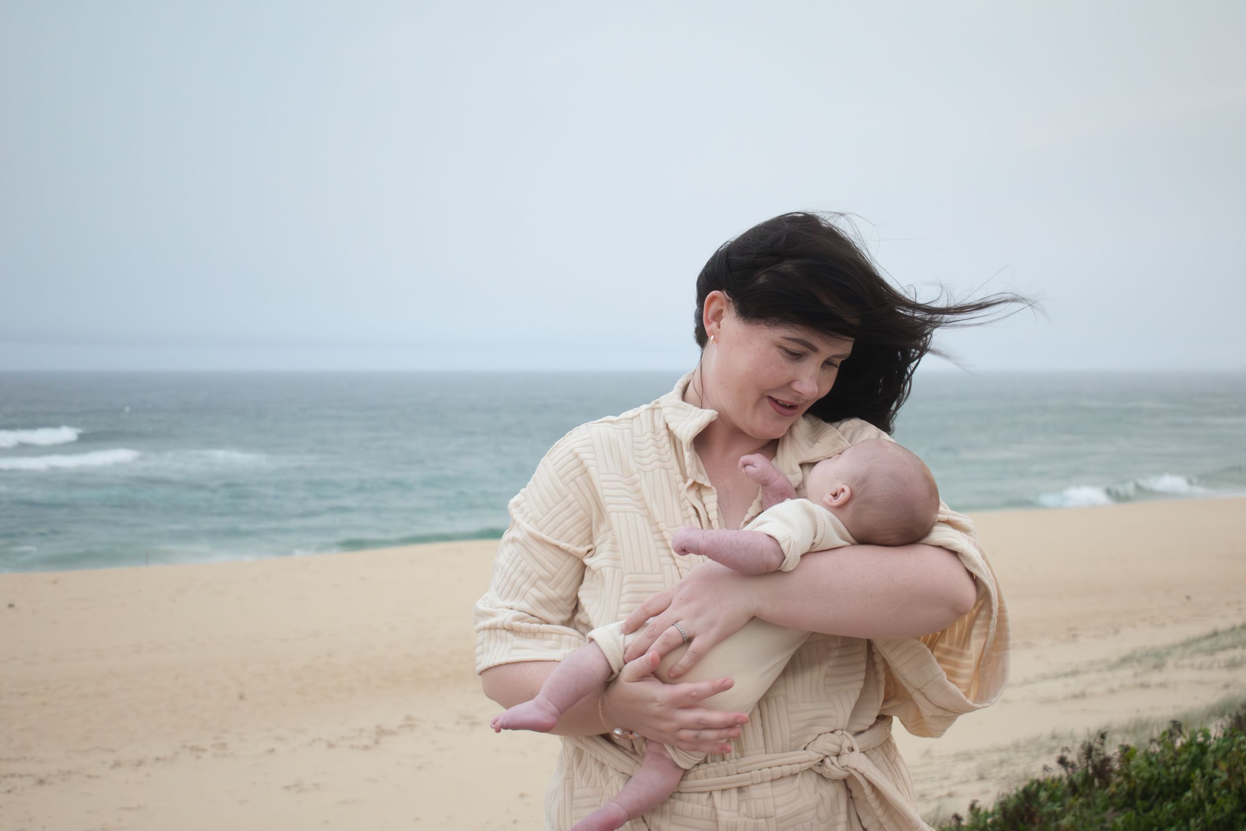 Newcastle newborn baby photographer capturing new mother holding baby at the beach