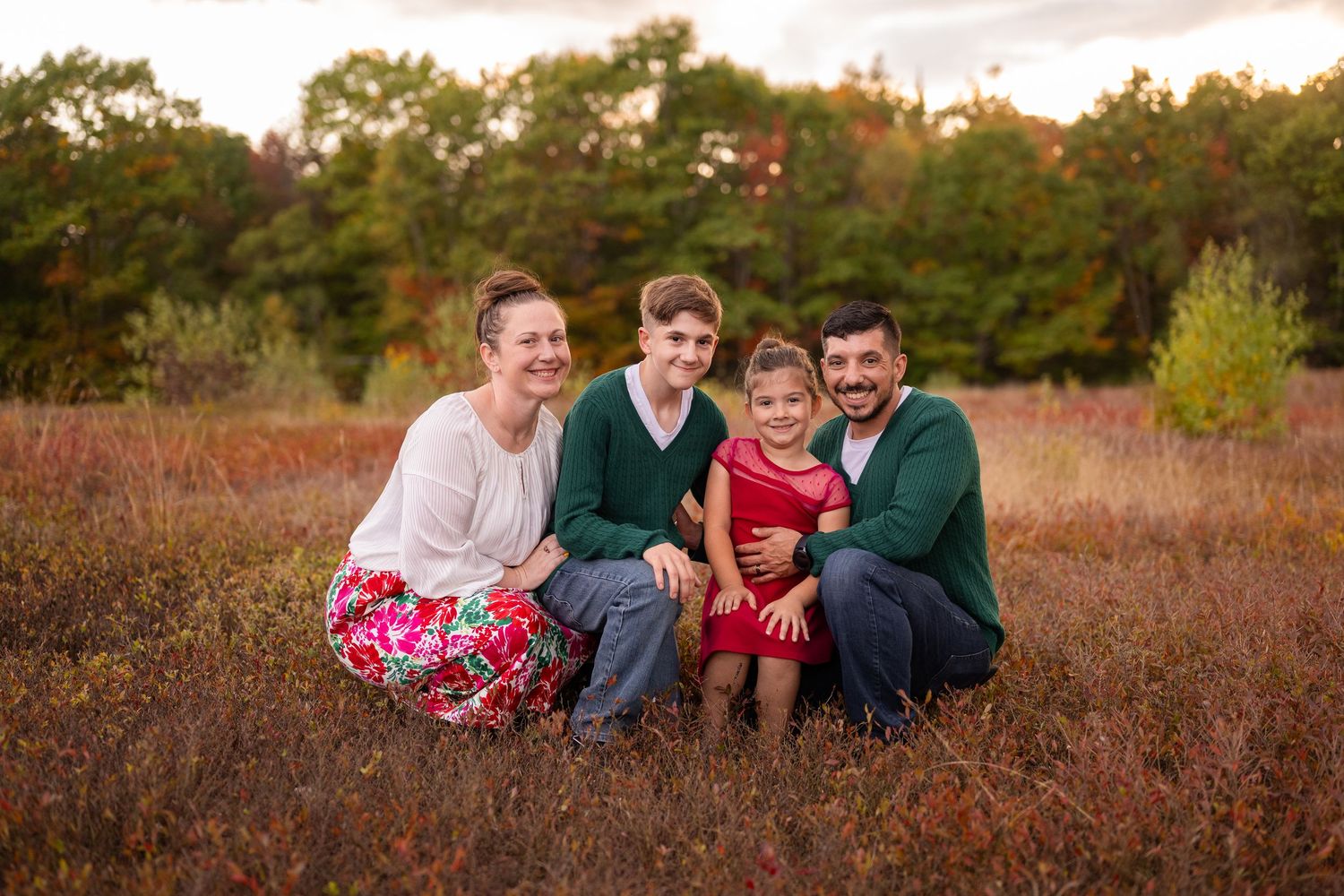 Family sitting together in a rustic autumn field at sunset with warm golden light and tall grass.