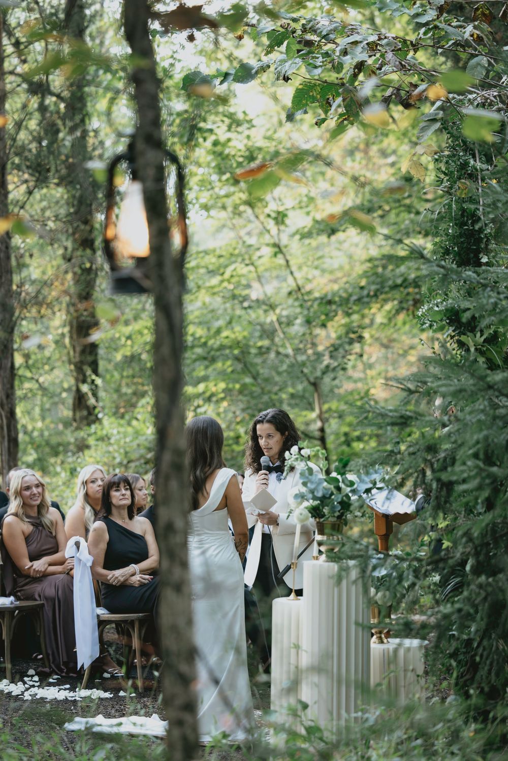 Wedding guests gather in a serene forest setting with white columns and natural greenery.