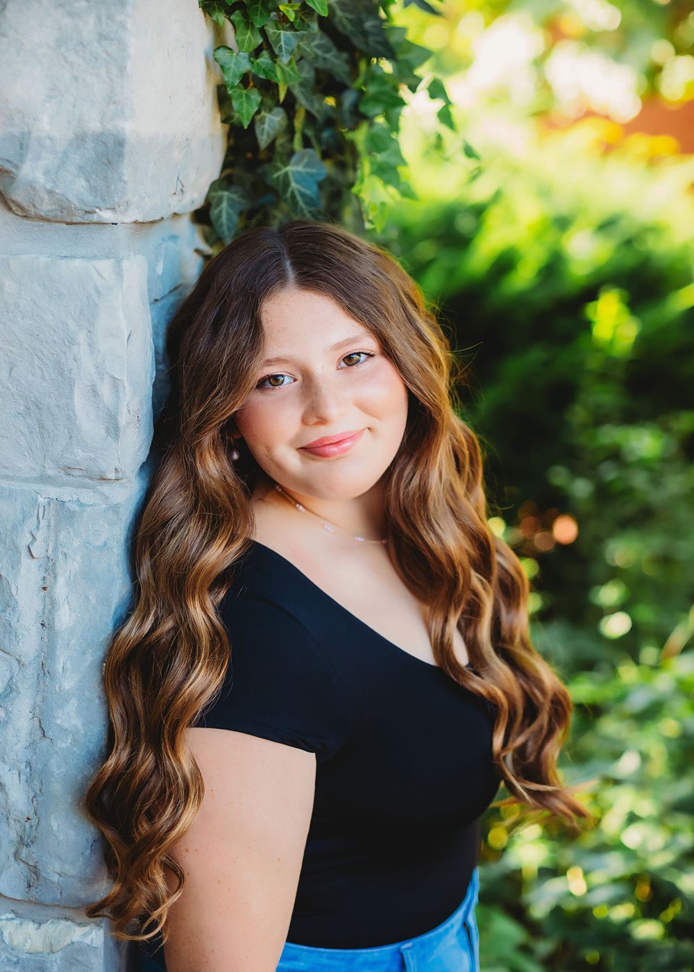 Portrait series featuring someone in a black top against a stone wall with lush greenery.
