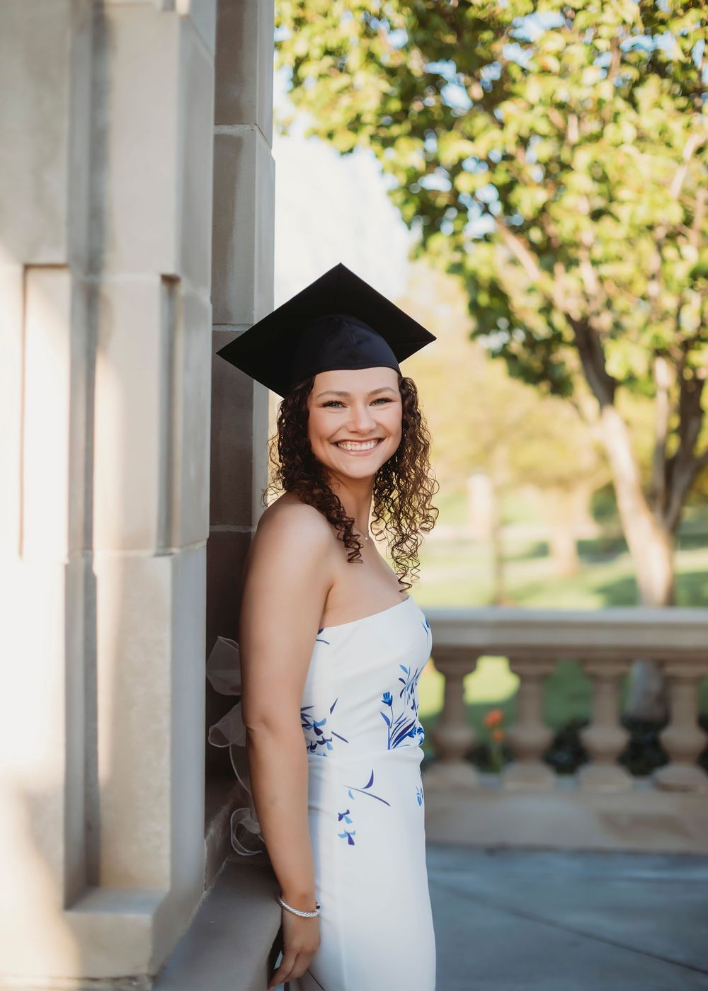 Graduate in cap and gown poses on campus during golden hour.