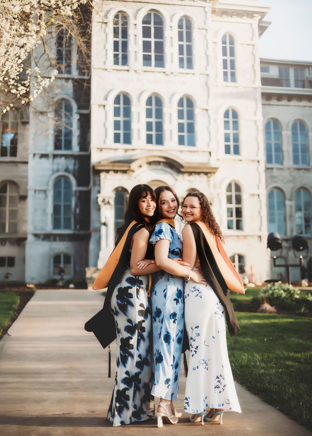 Friends in floral dresses pose together in front of a historic stone building.