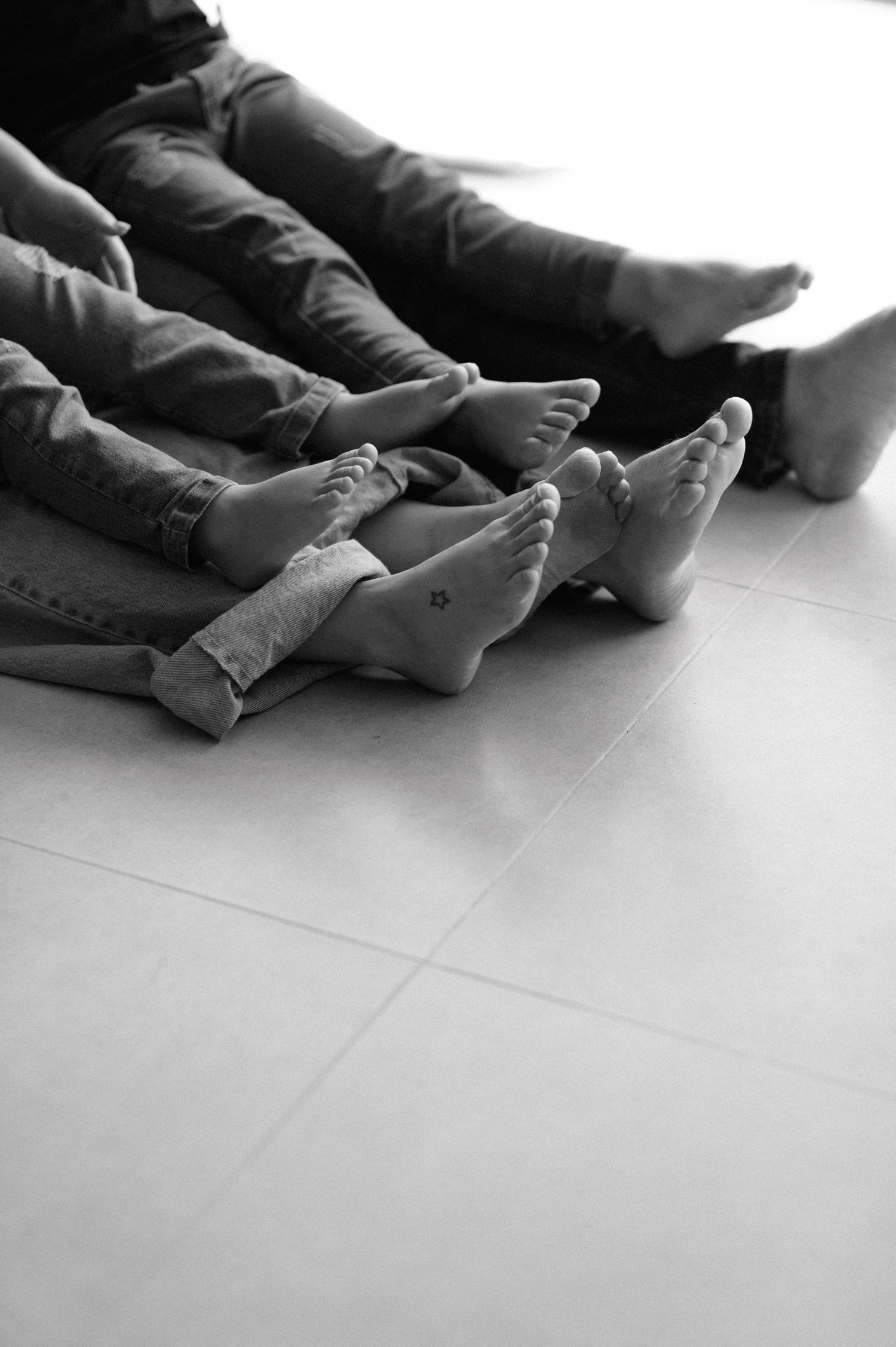 Black and white photo series showing a person in jeans and light top performing expressive dance movements against a plain wall.