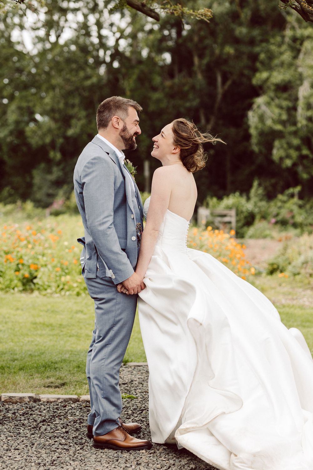A couple in wedding attire shares romantic moments in a garden setting with orange flowers in the background.