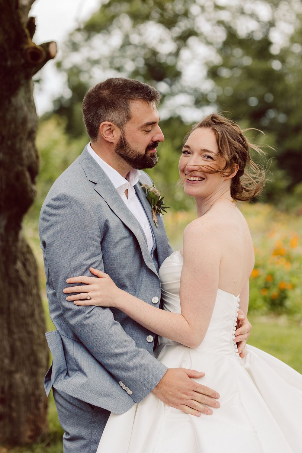 A couple shares a joyful moment together outdoors during their wedding, with the bride in white and groom in gray.