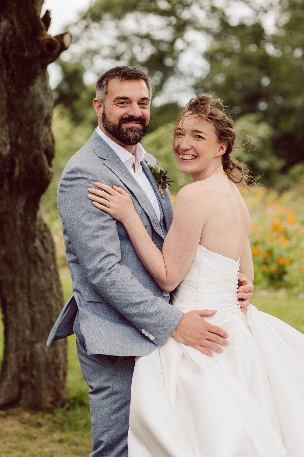 A joyful couple shares intimate moments during their outdoor wedding photoshoot in gray suit and white dress.