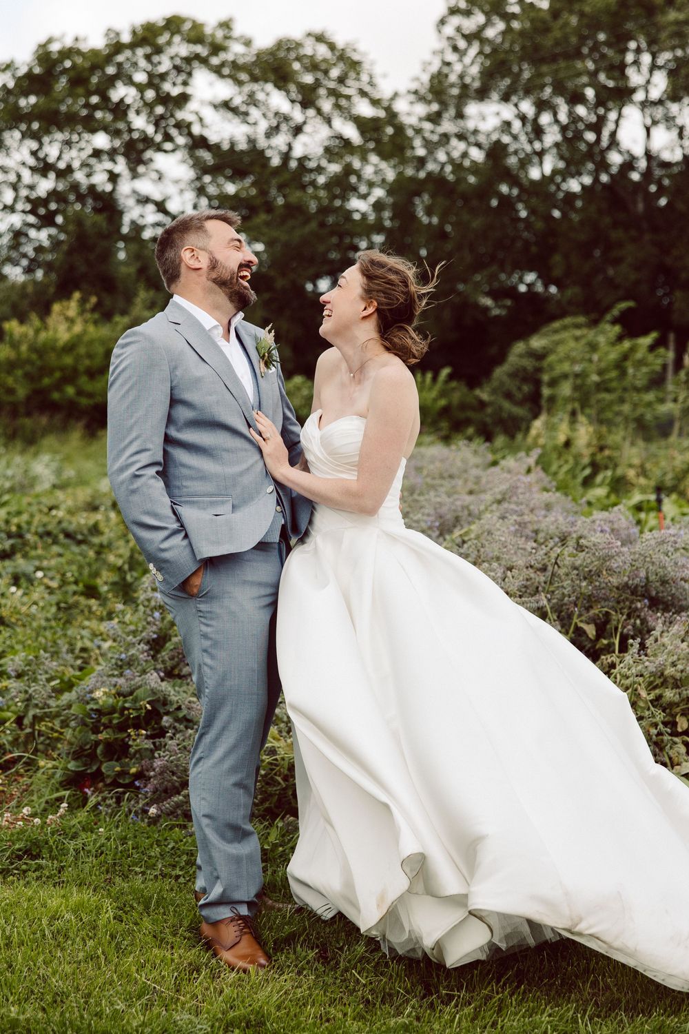 A joyful couple in wedding attire share a candid moment together in a lush outdoor garden setting.