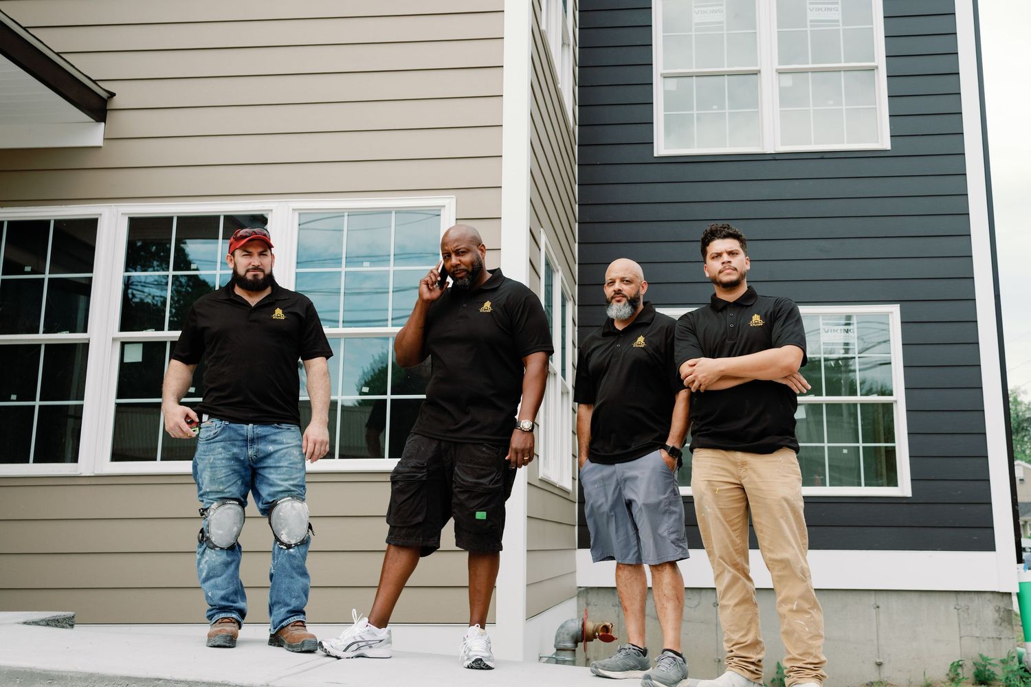 A series of people in black shirts and casual wear standing in front of residential homes.
