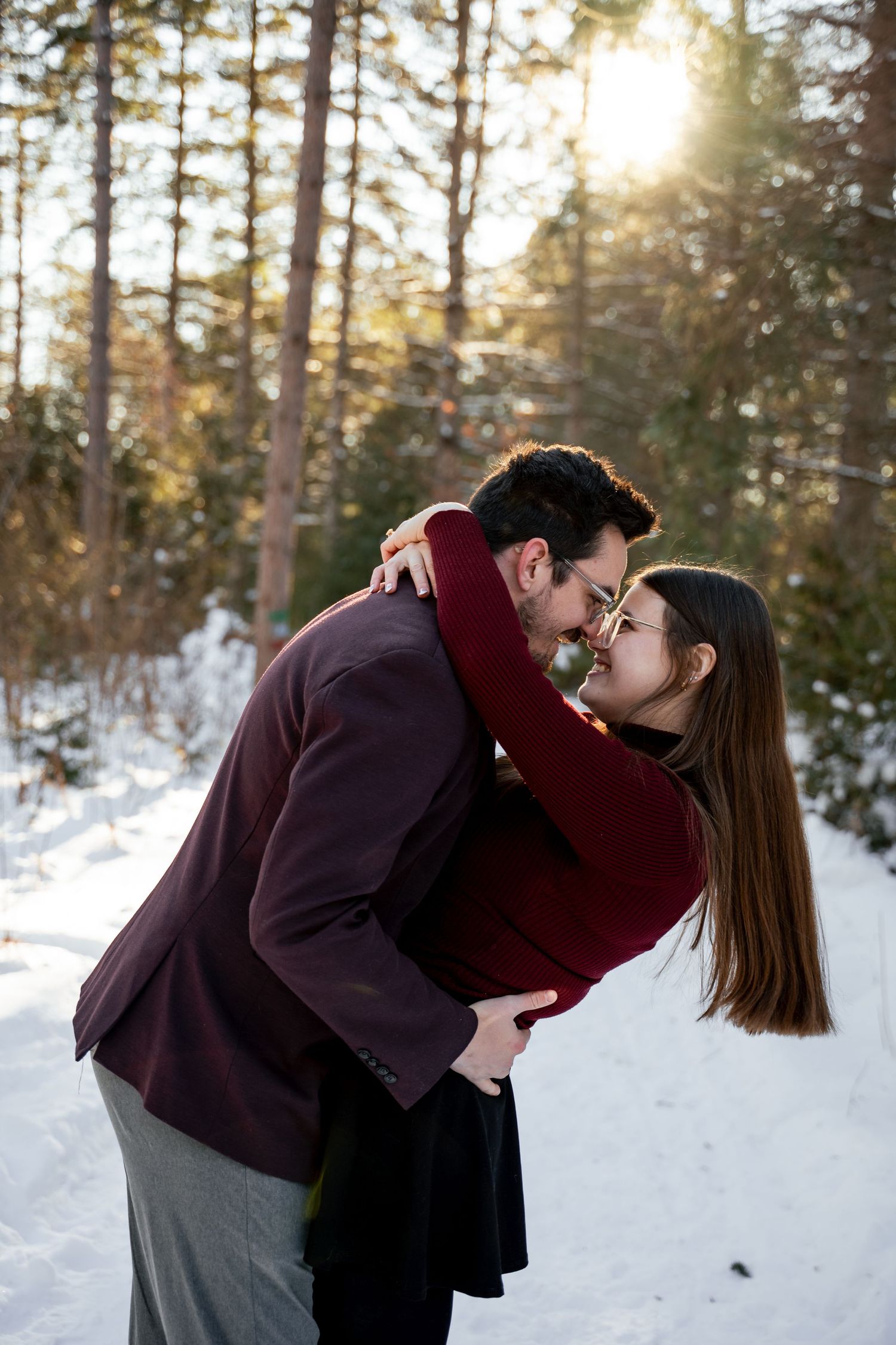 A romantic winter moment captured in a snowy forest setting with warm sunlight filtering through pine trees.