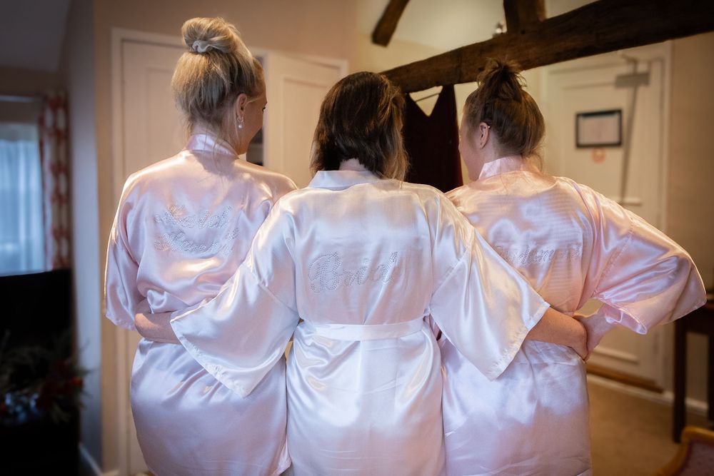 A row of bridesmaids in white satin robes getting ready for a wedding, shown from behind.