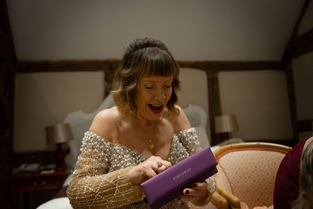 A person in a wedding dress laughs joyfully while getting ready in a sunlit room.
