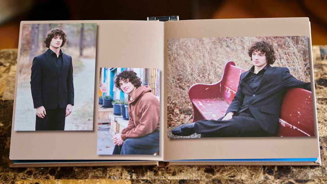Photo of male high school senior featured in linen album.  Senior is dressed in a black suit, sitting on a bench and standing on a pathway.