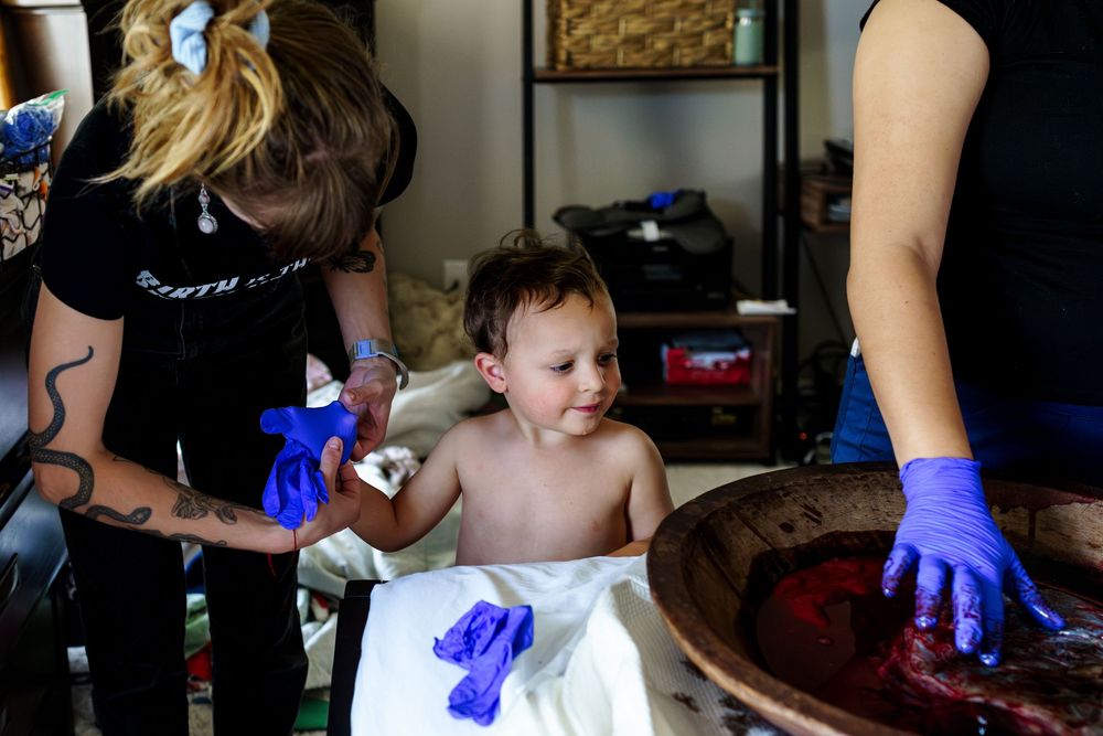 Healthcare provider wearing blue gloves examines a newborn baby on white cloth.