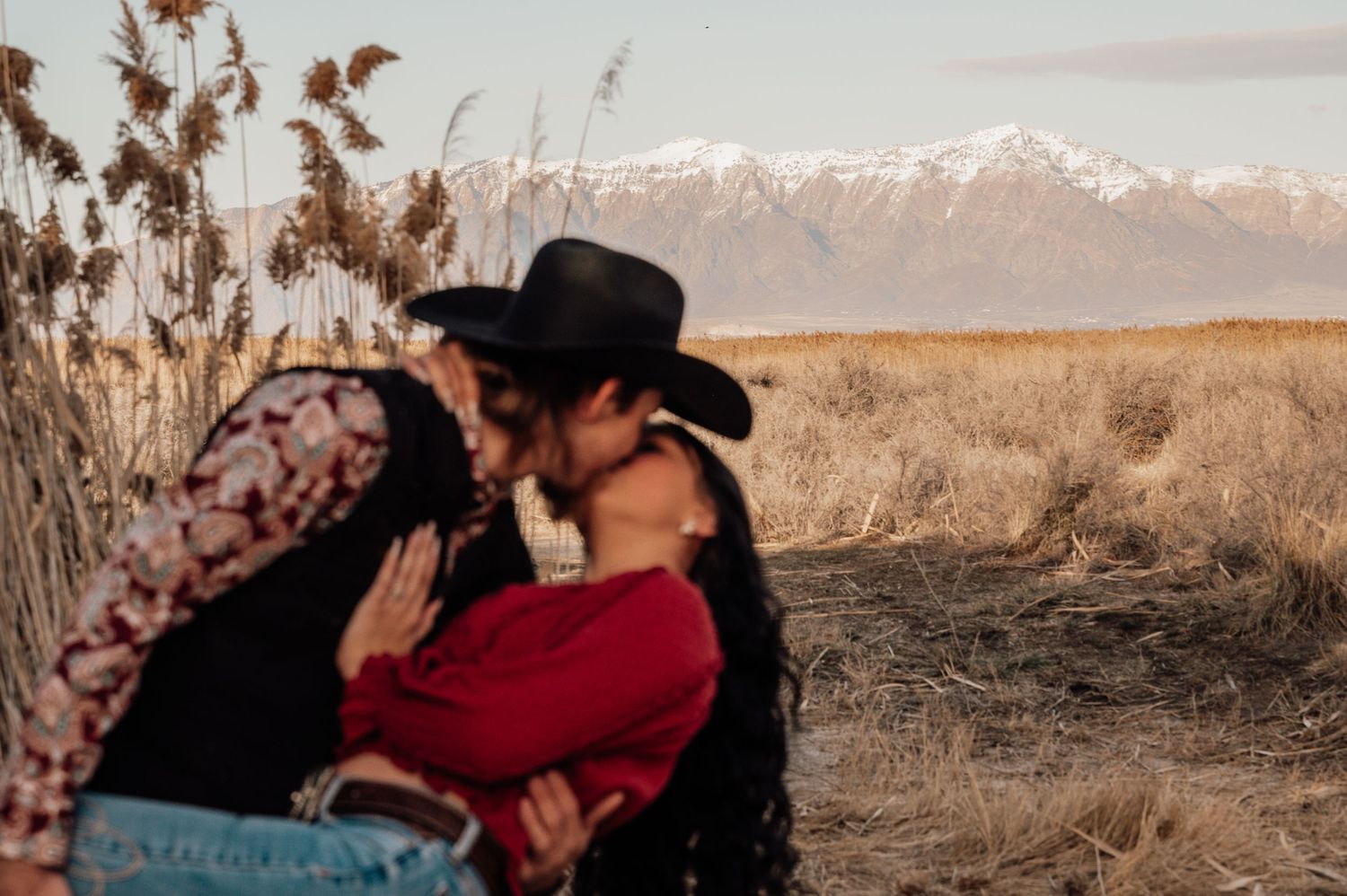 Couple embracing in rustic outdoor setting with mountain peaks in background.