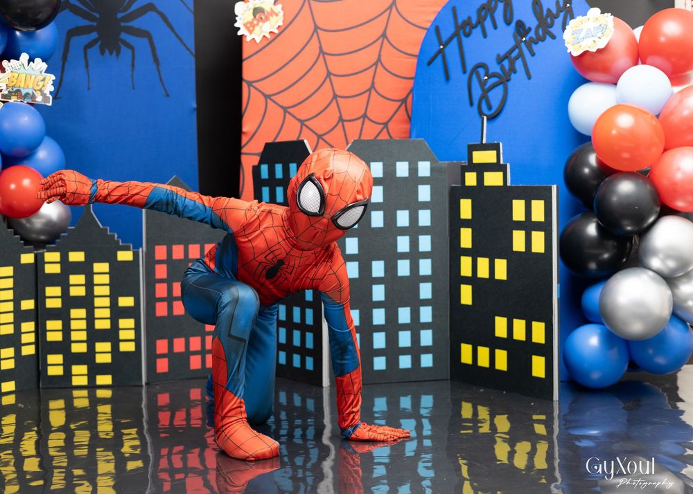 A Spider-Man themed party setup with a cityscape backdrop, balloon decorations, and web designs against a dark blue background.