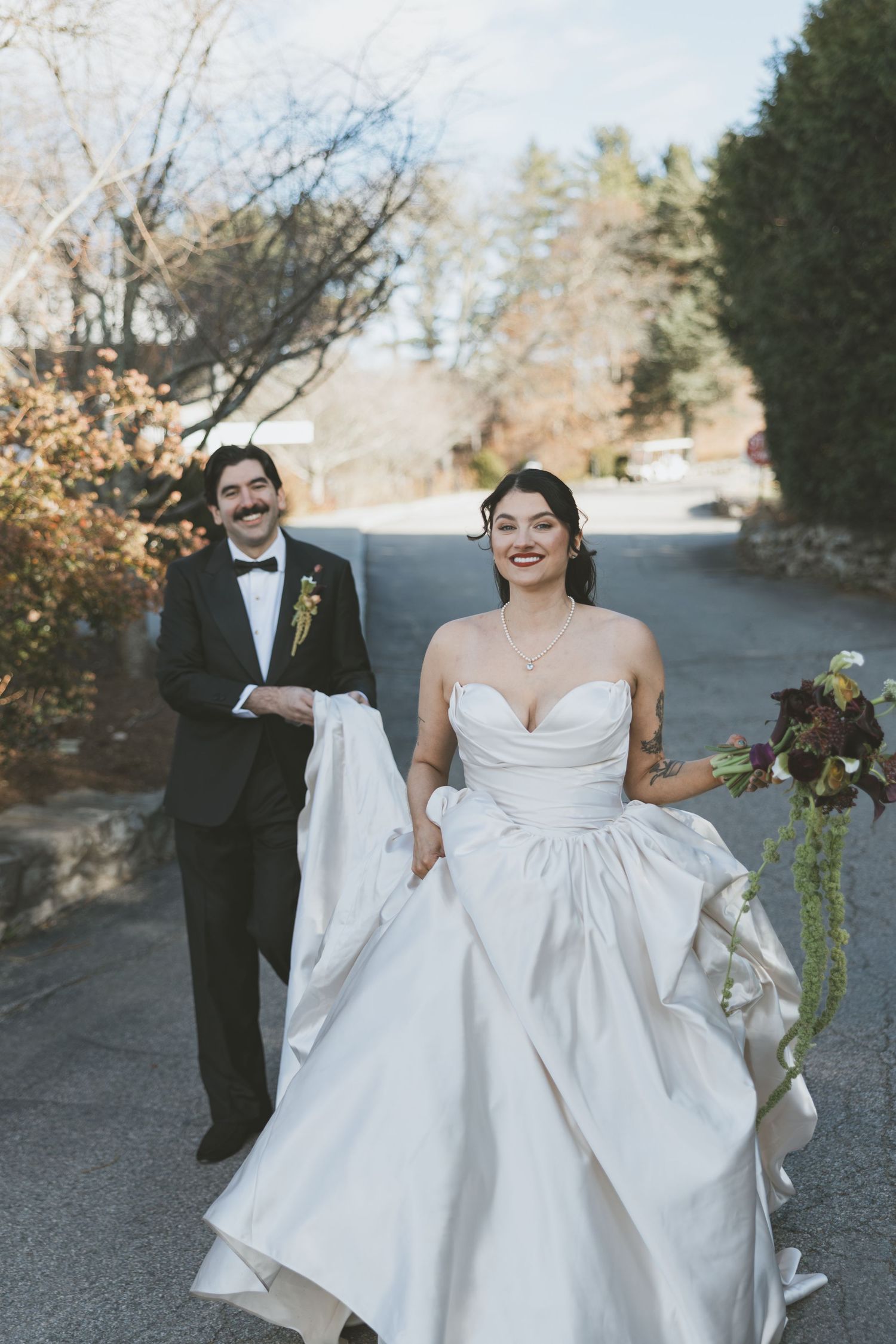 A couple walking down a road on their wedding day, with autumn trees in the background.