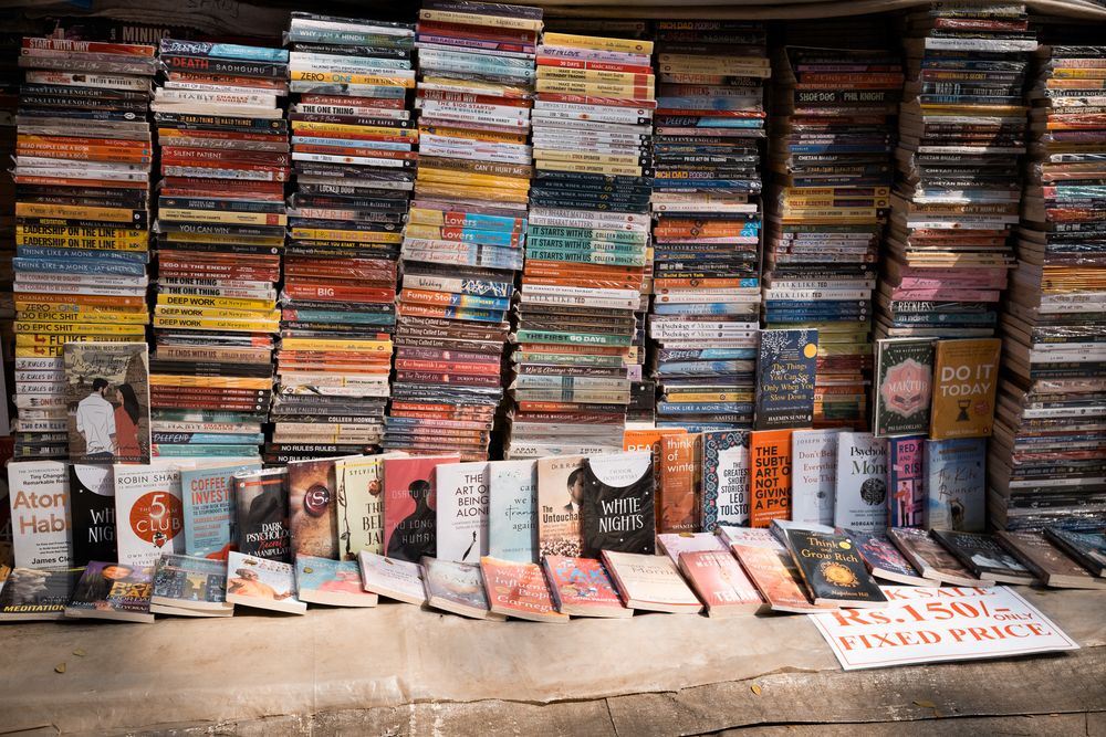 A street book stall displays stacked books and DVDs with a fixed price sign.