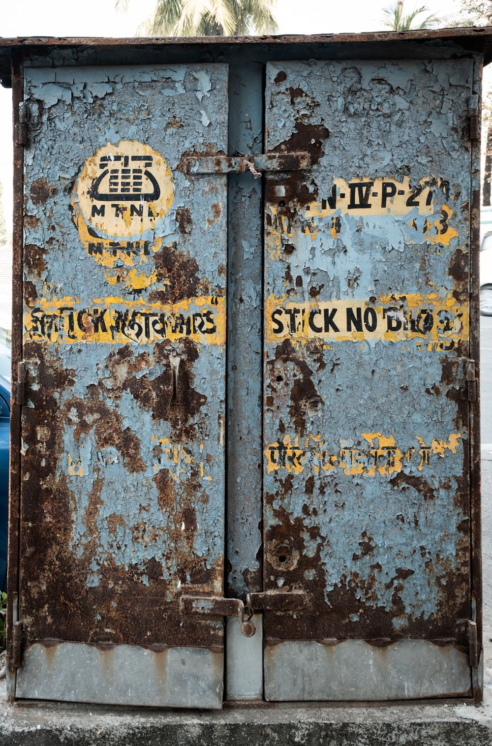 Rusty blue metal doors with MTNL logo and Stick No Bills warning painted in yellow.