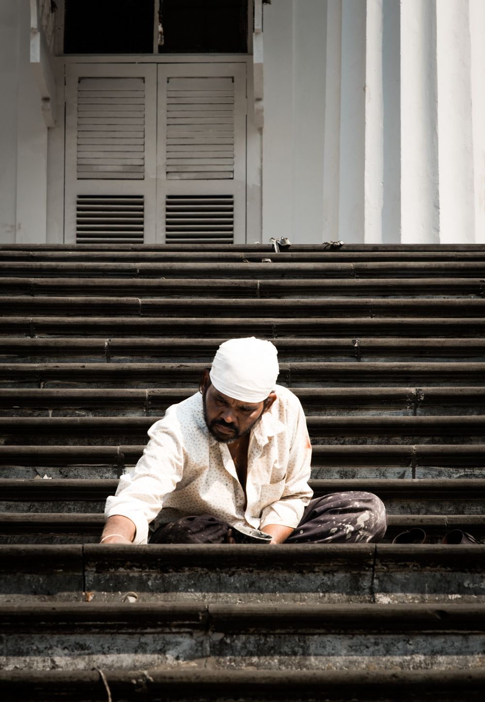 Indian man in white kurta and turban sitting cross-legged on stone steps reading.