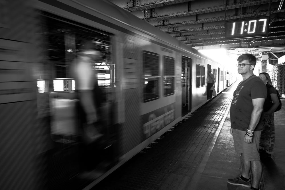 Black and white photo of a man standing on a platform as a train speeds past at 11:07.
