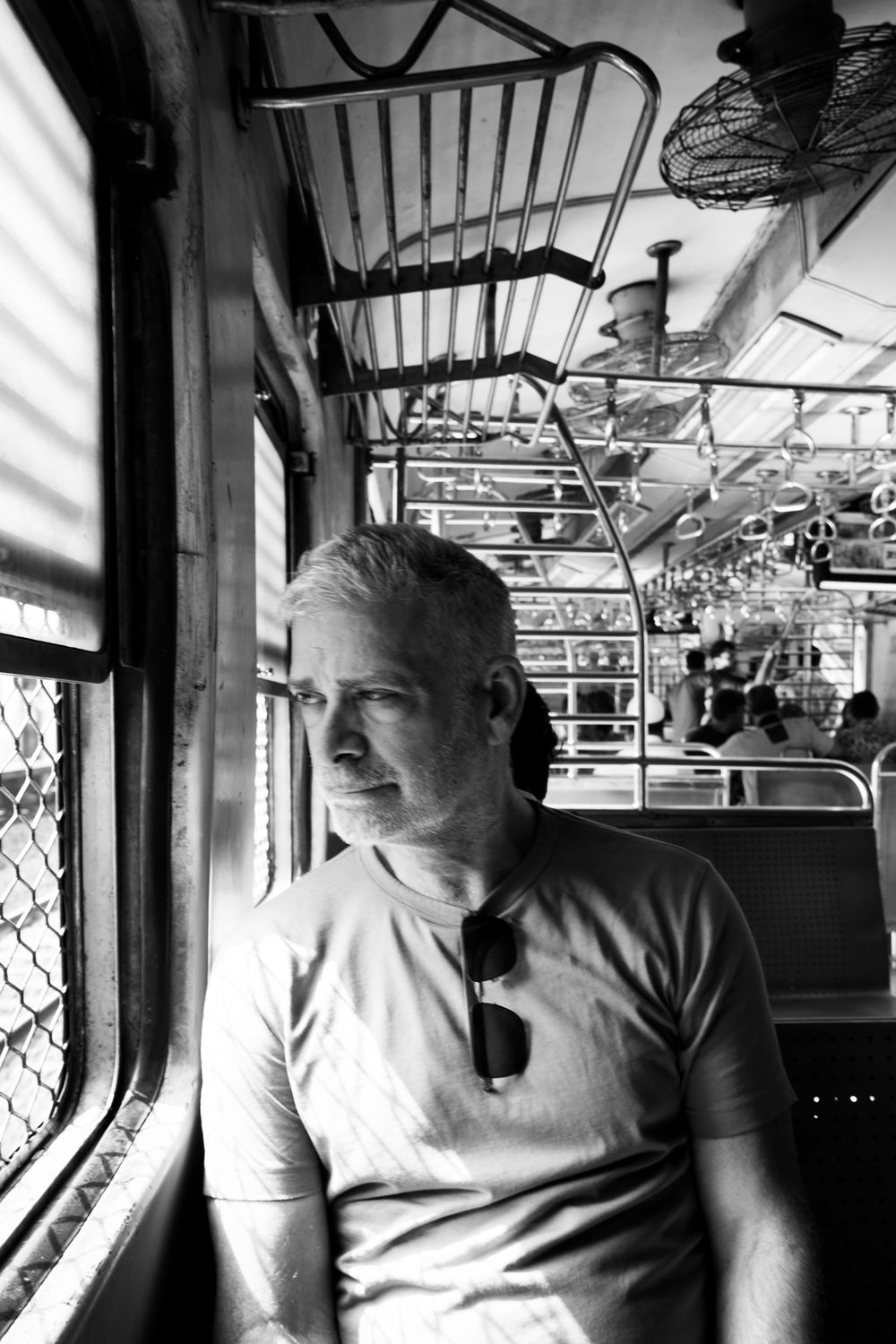 Black and white portrait of a middle-aged man sitting by a window inside a vintage Indian train.