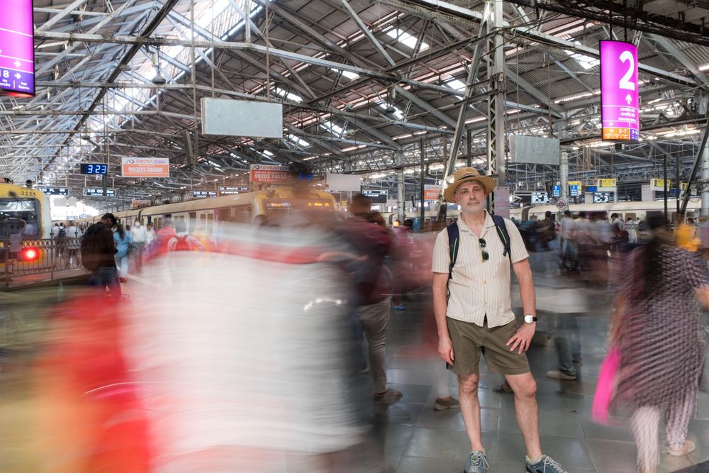 Tourist standing still amid motion-blurred commuters inside a busy Mumbai railway station.