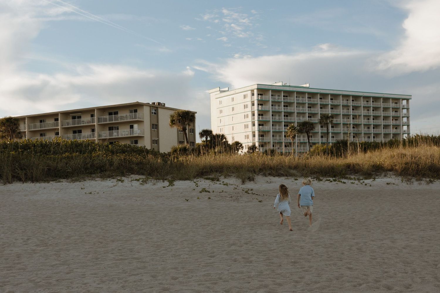 People enjoying a sunny day walking and playing along a scenic beach shoreline with waves and sand.
