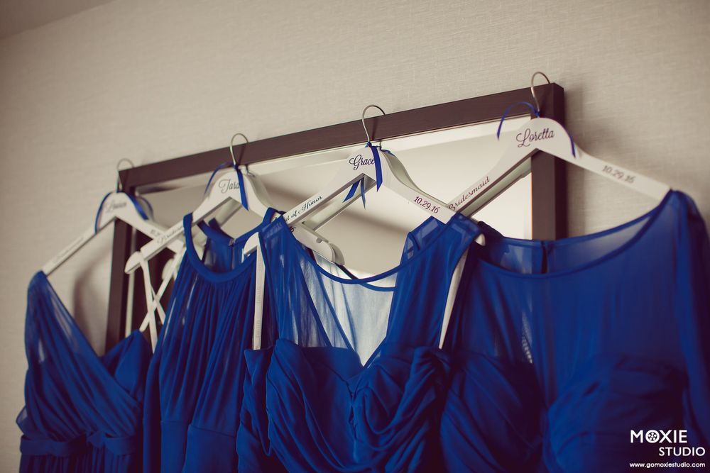 A row of royal blue bridesmaid dresses hanging on white hangers against a beige wall.