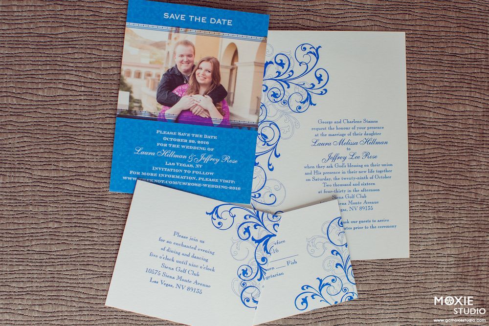 Wedding invitation suite with blue and white cards featuring elegant floral designs laid out on a wooden surface.