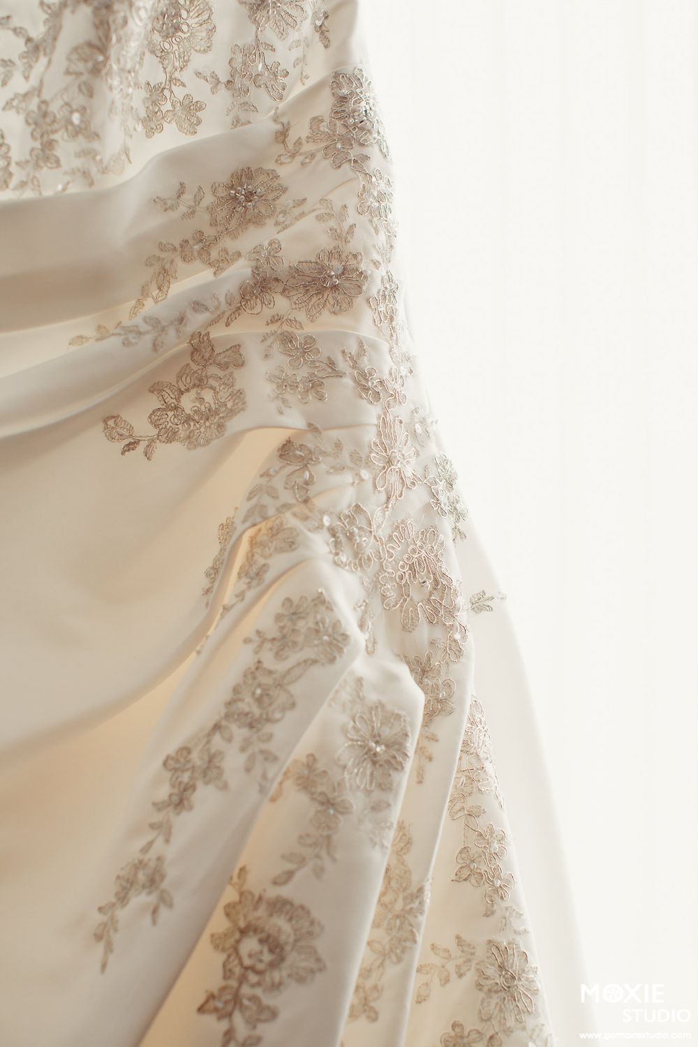 Close-up detail of an elegant white wedding dress with delicate floral lace embroidery and gathered fabric.