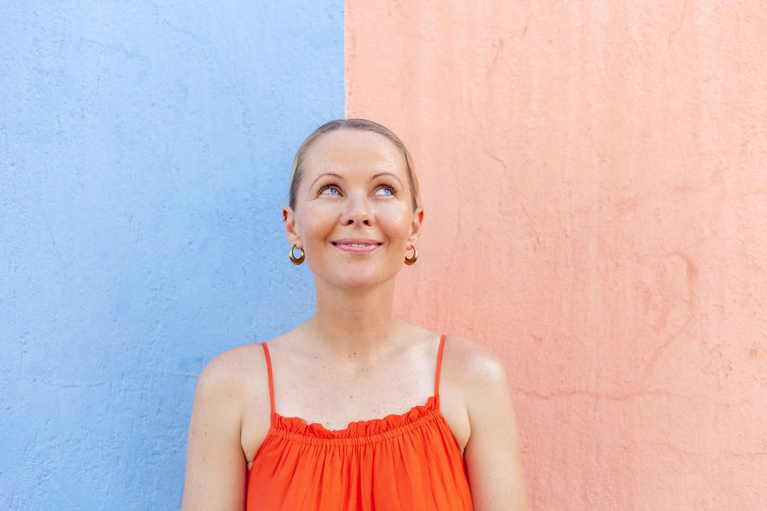 Woman in bright orange top posing against pink and blue wall background.