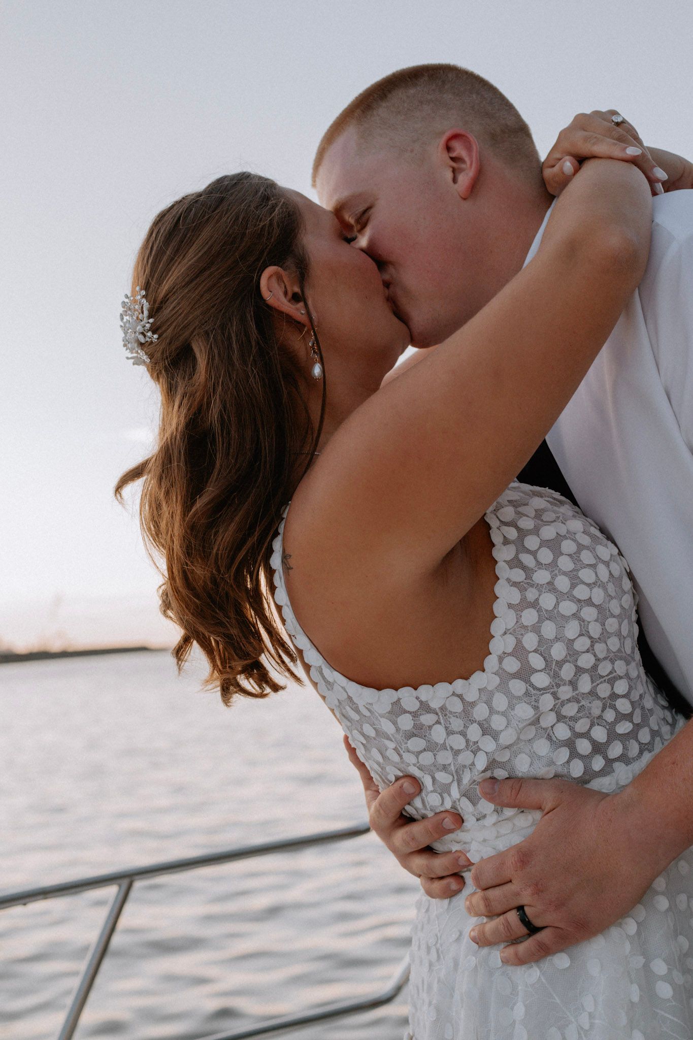 Bride and groom sharing a passionate kiss on a boat at sunset on the water.