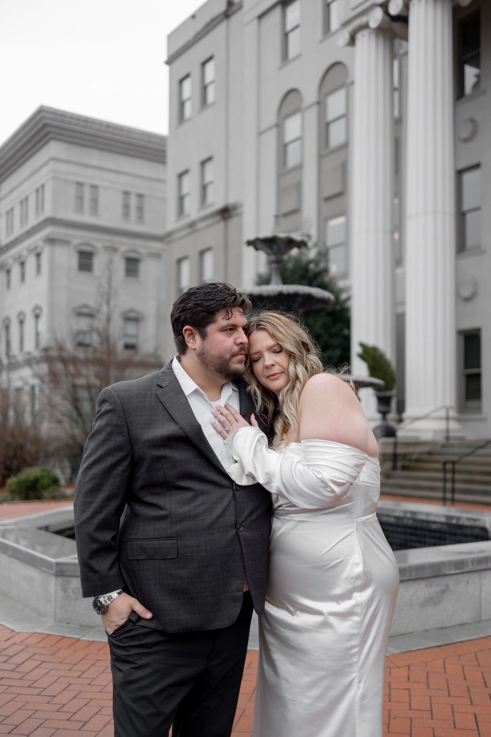 A romantic couple shares a tender moment on the steps of a grand white columned building.