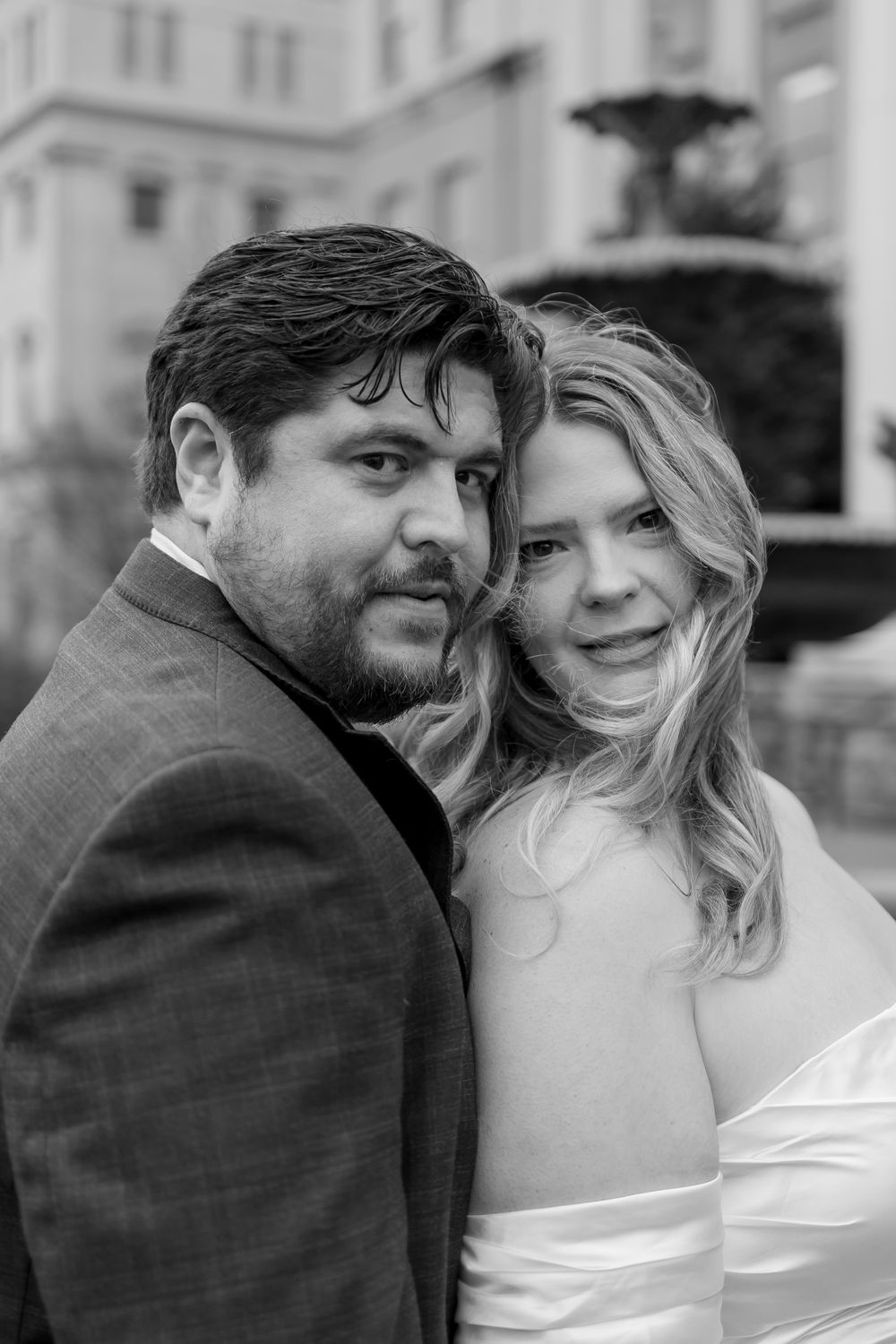 A couple shares intimate black and white wedding portraits in an outdoor setting with architectural details visible.
