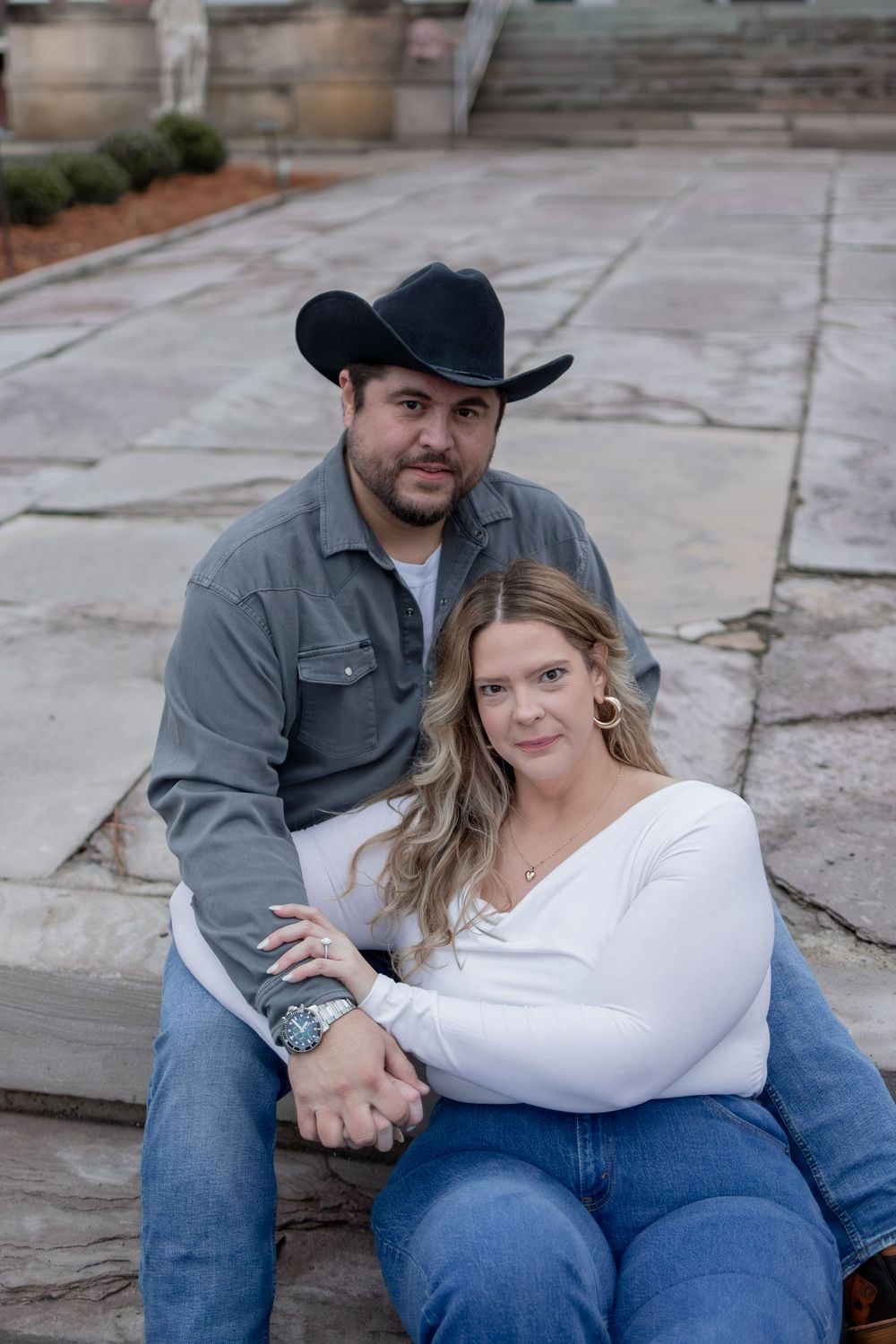 A couple in casual attire poses together on stone steps during an outdoor photo session.