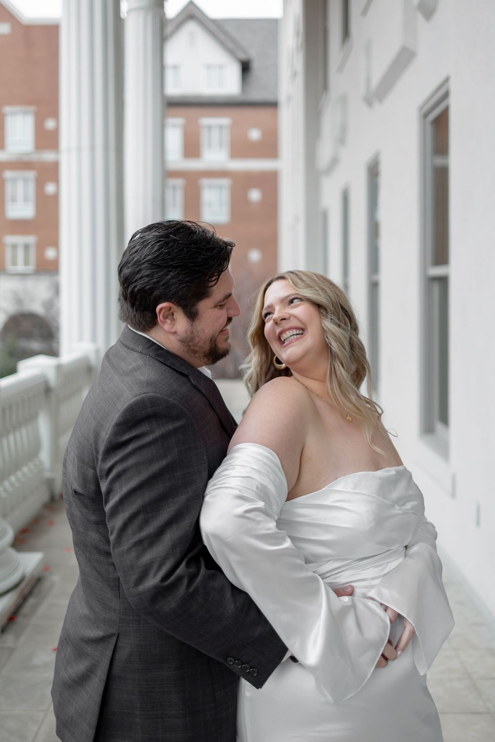 A romantic couple in wedding attire share intimate moments along a bright white columned porch.