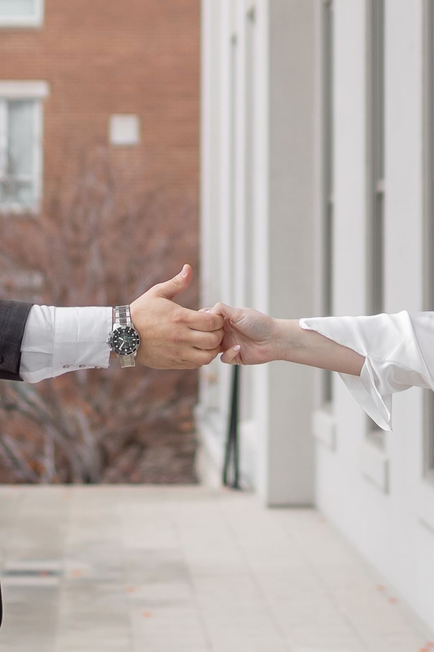 Two hands reach out from opposite sides of a white porch railing, passing a small object between them.